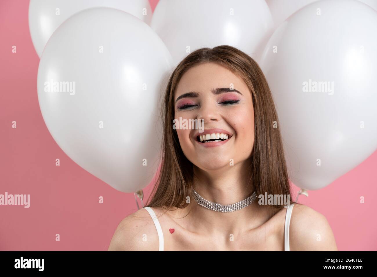 Positiva, ragazza sincera sorridente su uno sfondo di palloncini e sfondo rosa. Una bella signora di buon umore aspetta la vacanza, positivo, peccato Foto Stock