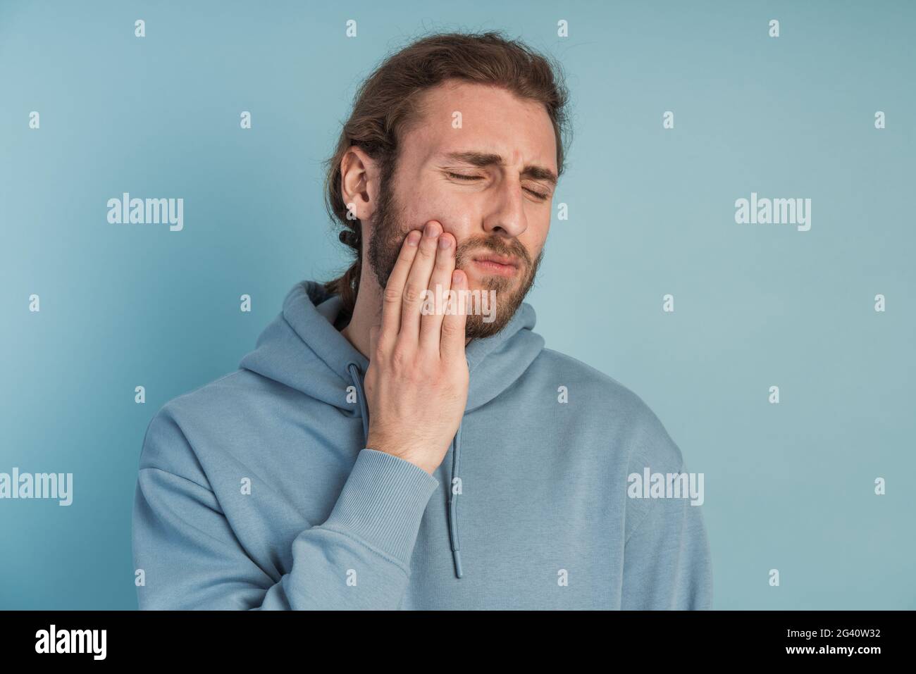 Dolore ai denti. Giovane uomo che sente dolore, che tiene la guancia con entrambe le mani, che soffre di mal di denti, che ha un'espressione dolorosa Foto Stock