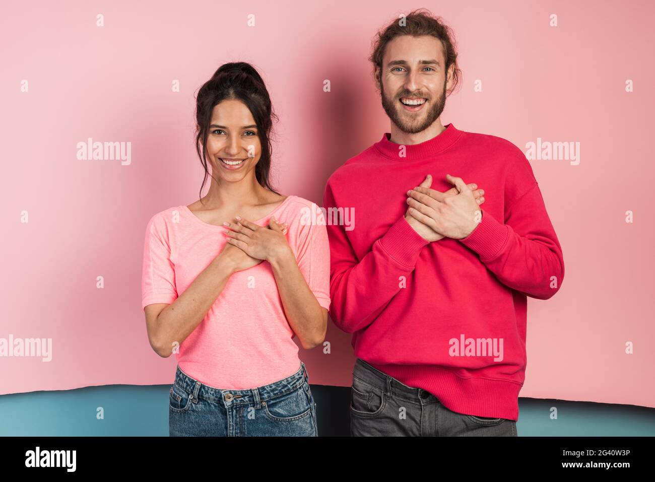 Bel ragazzo e ragazza che tocca il petto con le mani, mostrando un gesto dal cuore. Coppia carina su sfondo rosa e blu. Foto Stock