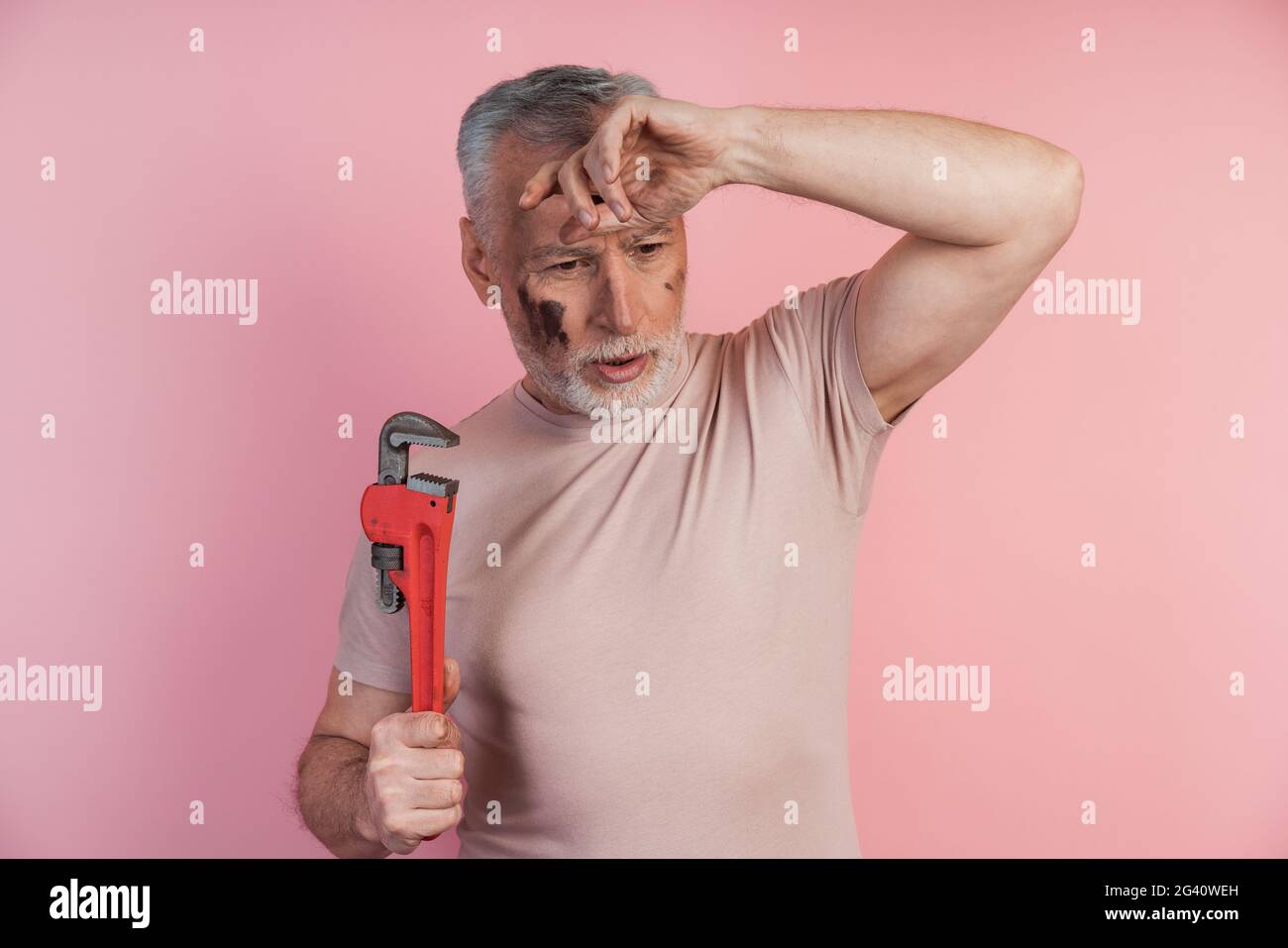 L'uomo stanco con una chiave in mano gli afferrò la testa. Uomo isolato su sfondo rosa, stanco di lavoro, uomo stanco con una chiave in mano afferrato Foto Stock