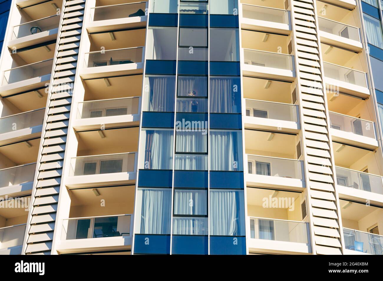 Un primo piano delle finestre di un alto edificio a più piani in blu e beige con balconi con vetri. Foto Stock