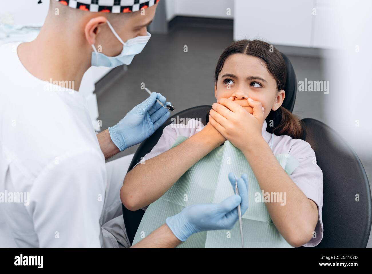 La bambina ha paura del dentista e cura i denti. In una sedia dentale, la ragazza copre la bocca con le mani. Foto Stock