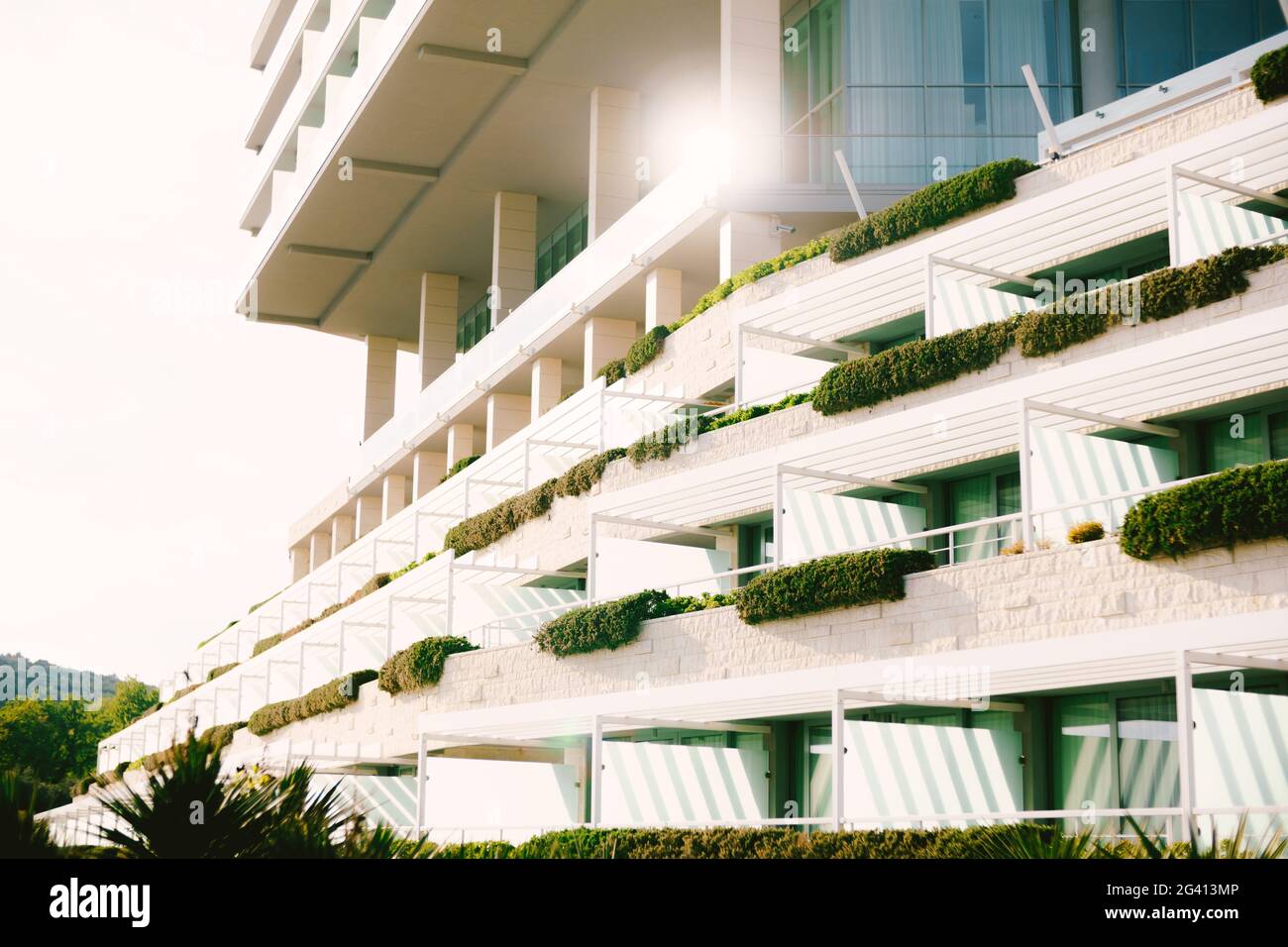 Grande hotel con grandi balconi continui e colonne con vegetazione in una giornata di sole. Foto Stock