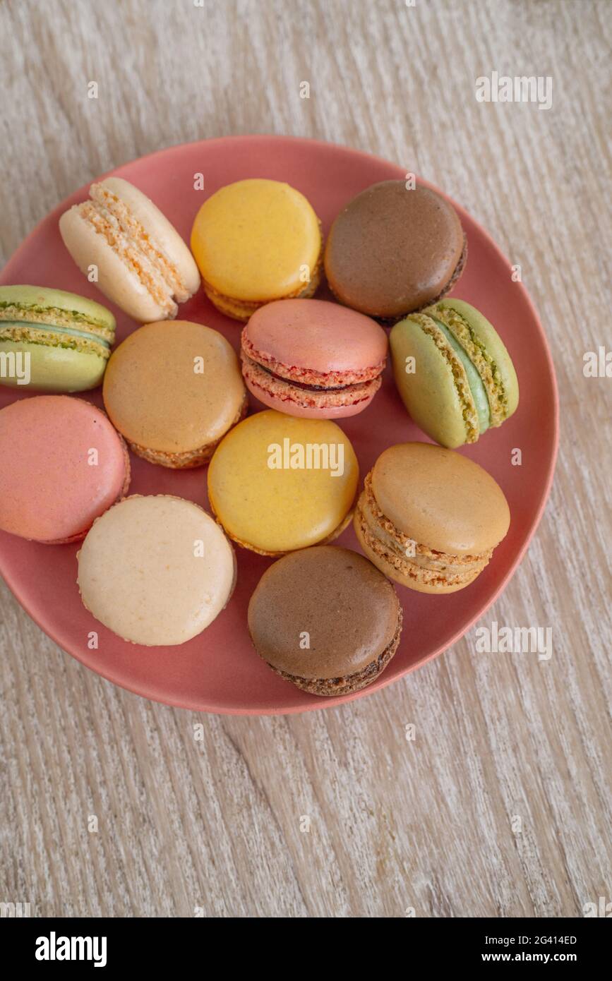 Macarons vista dall'alto su piatto rosa su sfondo di legno, dolci retrò carino. Selezioni di macaron color pastello Foto Stock