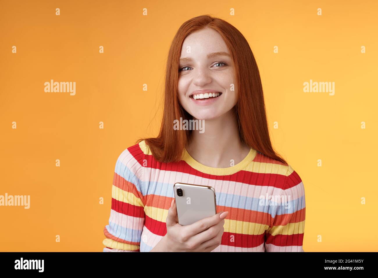 Amichevole entusiasta giovane ragazza rosso occhi blu utilizzando smartphone girare la fotocamera rispondere sorridendo ampiamente dicendo chi ha inviato il messaggio Foto Stock