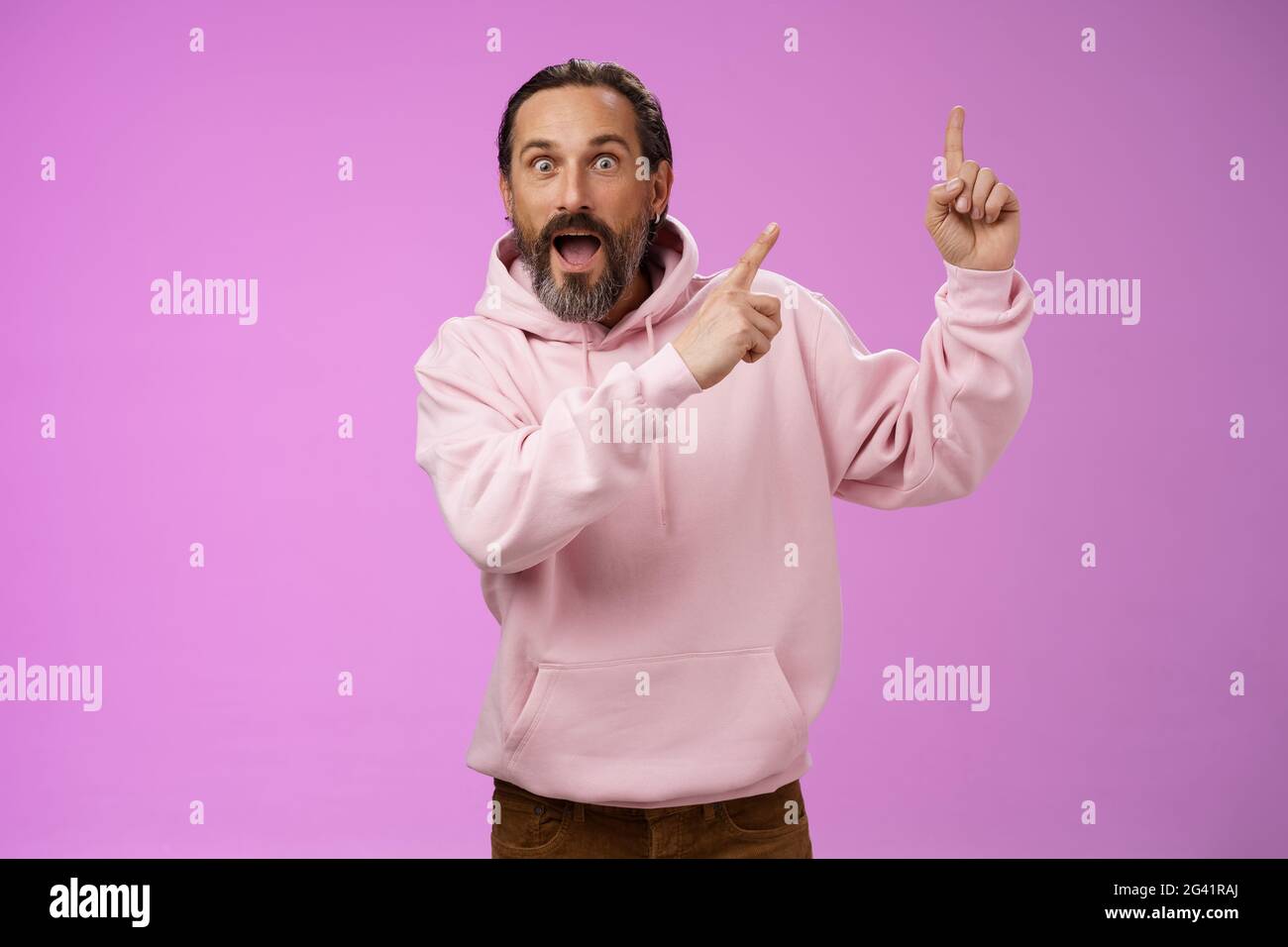 Impressionato scioccato scosso fresco hipster maturo 50s uomo bearded capelli grigi in rosa felpa con cappuccio retelling incredibile storia che punta in su Foto Stock