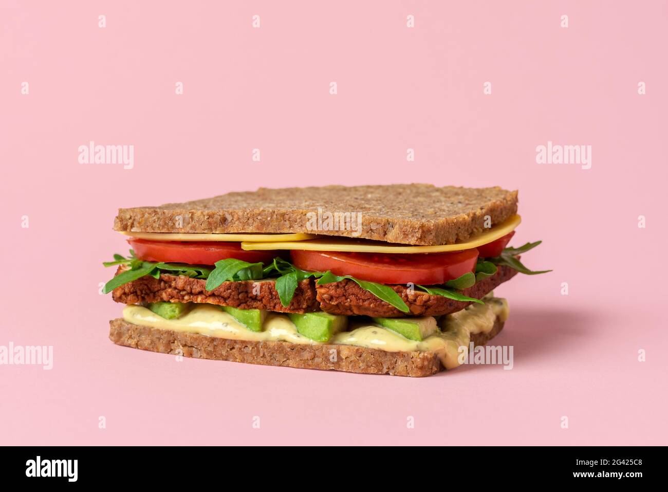 Sandwich sano senza carne con ingredienti vegani e verdure fresche. Sandwich a base di piante con tofu affumicato, formaggio vegano, avocado, remoulade, pomodoro Foto Stock