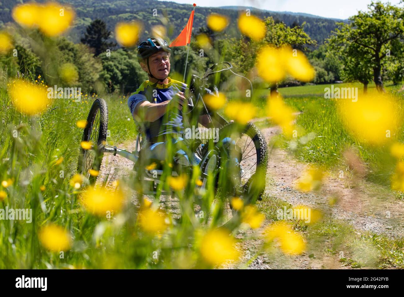 L'uomo guida una bicicletta per paraplegici su una strada sterrata attraverso un lussureggiante prato primaverile, Heimbuchenthal, Räuberland, Spessart-Mainland, Franconia, Baviera, Germ Foto Stock