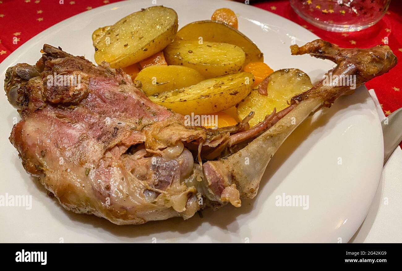 Primo piano di gustosa gamba di carne di agnello cucinata al barbecue servita in un elegante ristorante. Una deliziosa capra su un barbecue con patate e carote sul piatto. Griglia Foto Stock