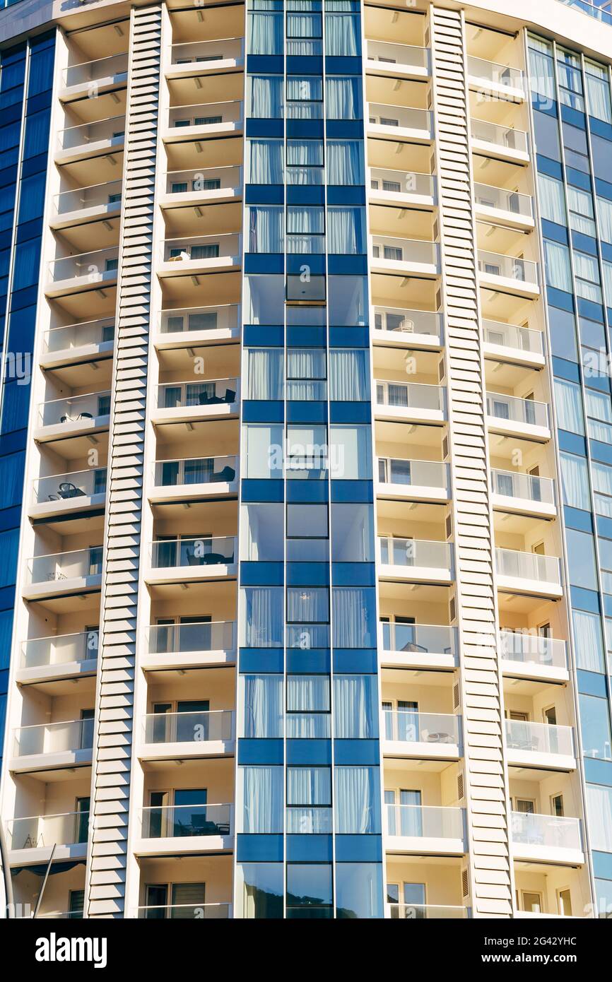 Alto edificio a più piani in blu e beige con balconi con vetri. Foto Stock