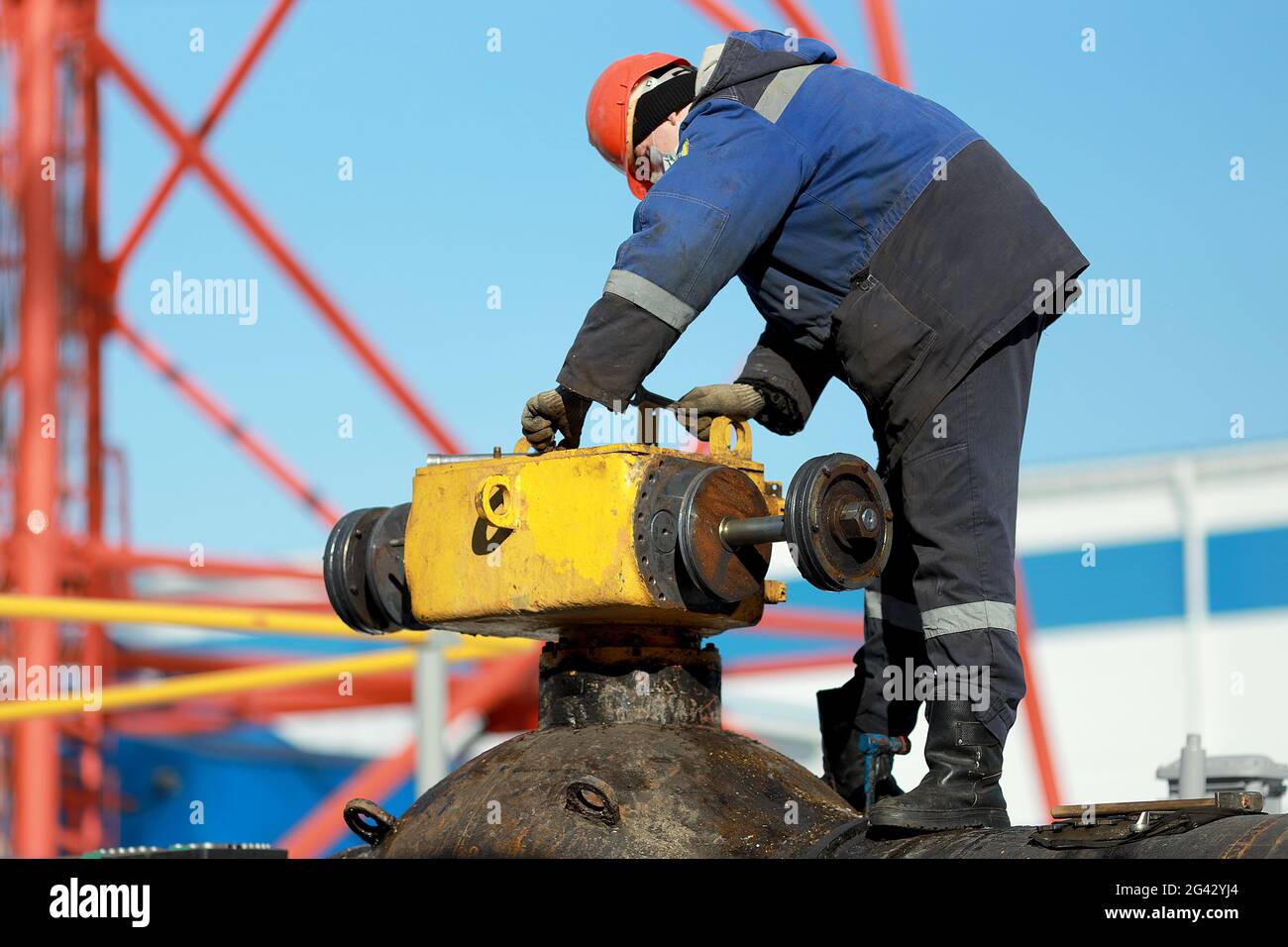 Un lavoratore in tute e un elmetto ripara una gru lineare del gasdotto principale sulla strada in inverno. Foto Stock