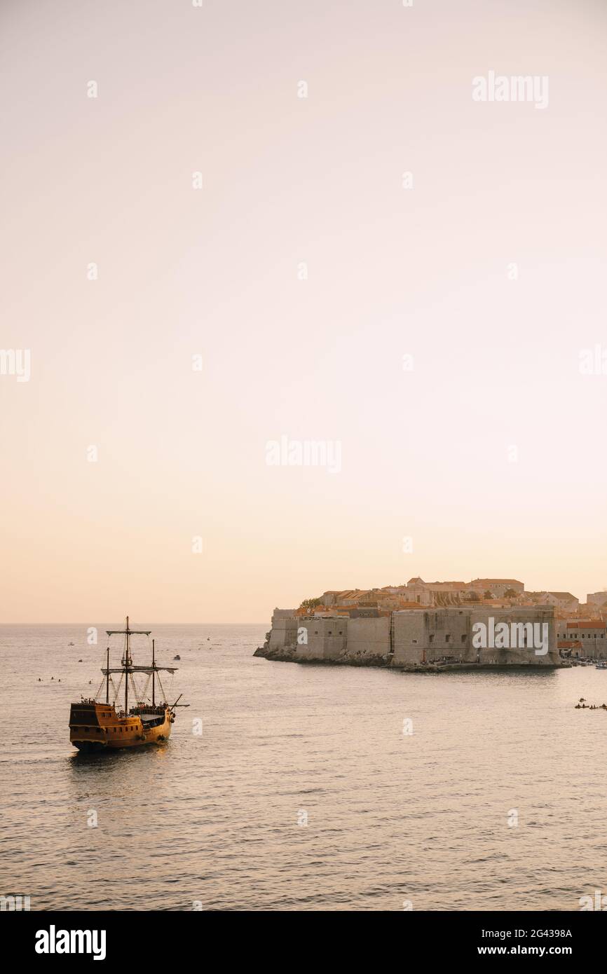 La città vecchia di Dubrovnik contro il cielo del tramonto. La nave a vela in legno Galleon si avvicina al molo principale di Dubrovnik. Foto Stock