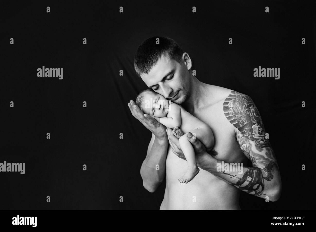Il padre con il tatuaggio sul braccio tiene la sua bambina neonato su uno sfondo bianco e nero Foto Stock