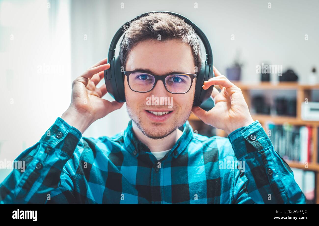 Ascoltare la musica a casa: Il giovane caucasico ascolta la musica con le cuffie. Maglietta blu controllata. Foto Stock
