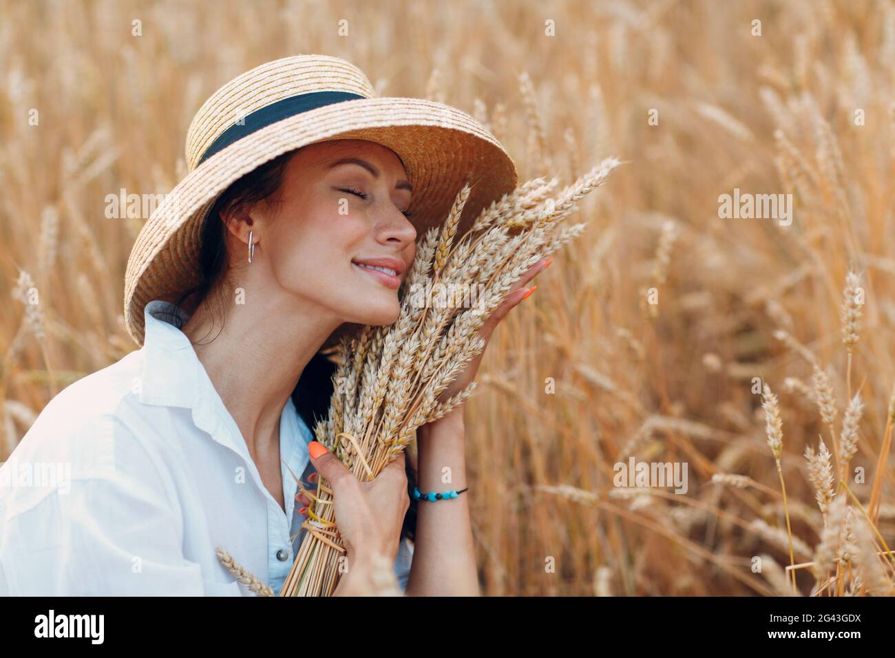 Giovane donna in cappello di paglia che tiene covoni di spighe di grano a campo agricolo Foto Stock