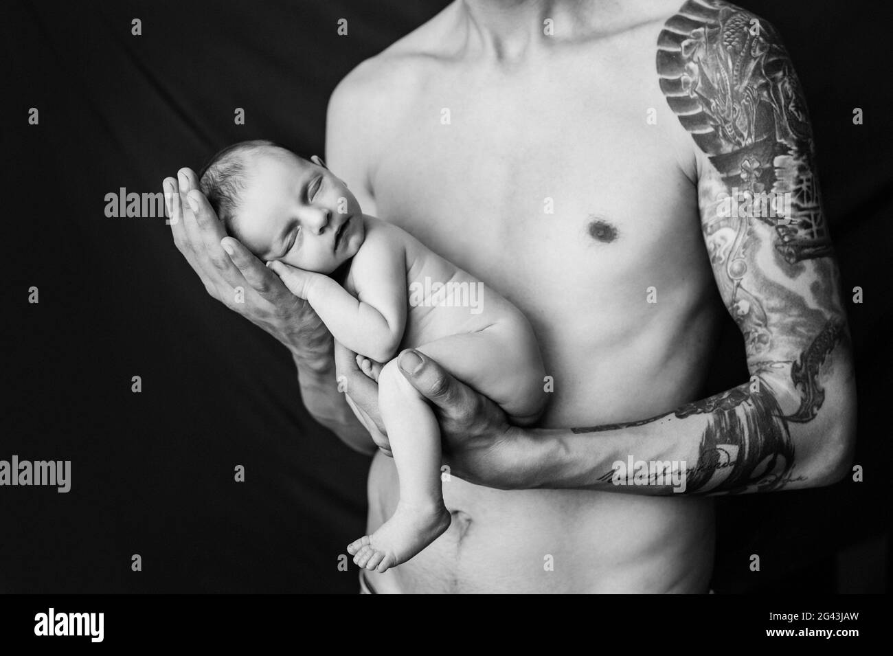Il padre con il tatuaggio sul braccio tiene il suo neonato su uno sfondo bianco e nero Foto Stock