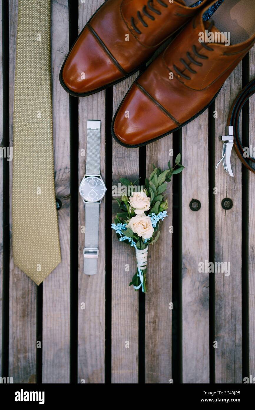 Dettagli matrimonio dello sposo - boutonniere, scarpe, cravatta e orologio su sfondo in legno, vista dall'alto. Foto Stock