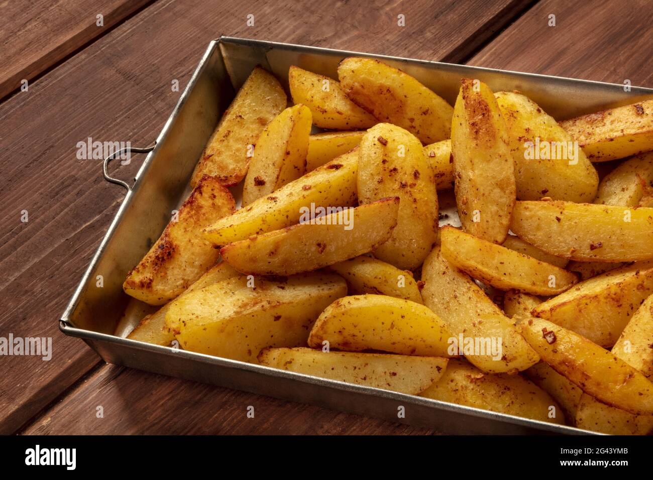 Spicchi di patate, tostati in forno, in una teglia su sfondo rustico Foto Stock
