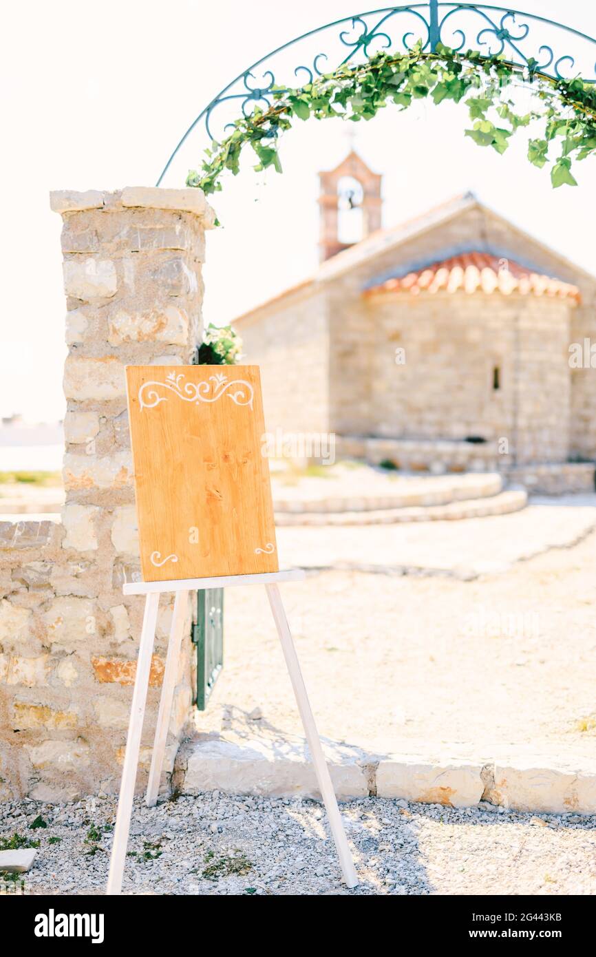 Cavalletto vuoto in legno con monogrammi in piedi su un cancello ad arco intrecciato con edera Foto Stock