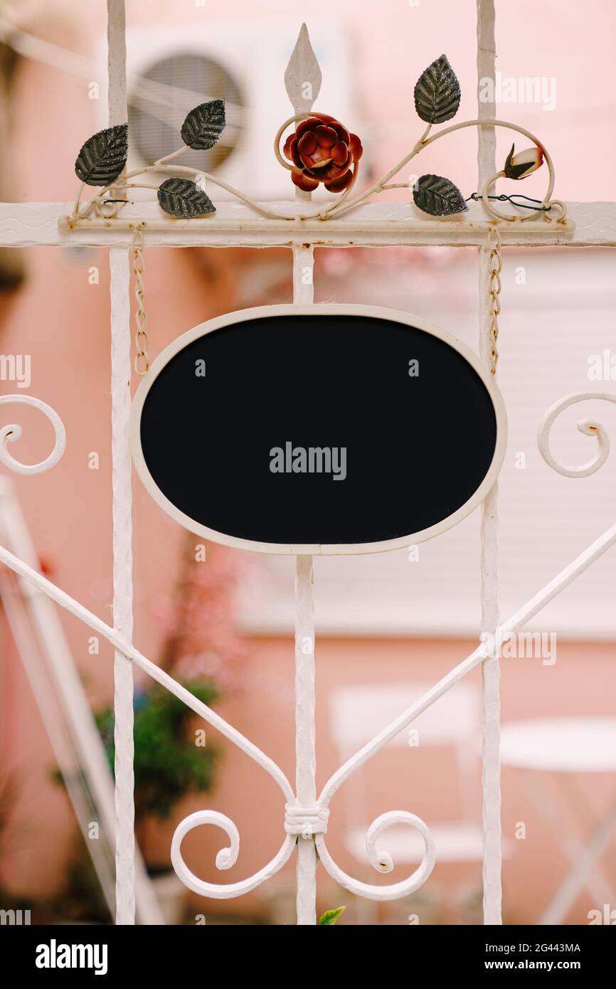 Vuoto segno ovale sullo sfondo di una bella forgiata recinzione bianca con fiori Foto Stock
