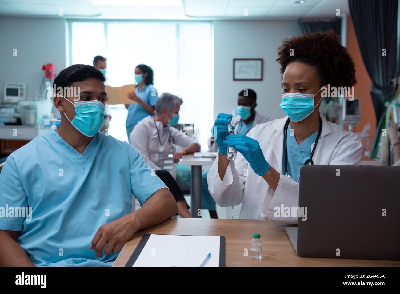 Corsa mista coppia di medici che indossano maschere di faccia che si preparano a. effettuare l'iniezione Foto Stock