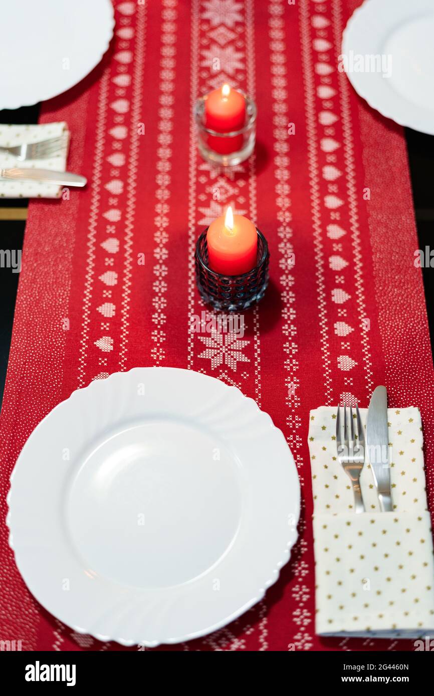 Decorazione festosa del tavolo per le feste di Capodanno con candele rosse e piatti bianchi su una tovaglia di stoffa rossa con patte a tema Foto Stock