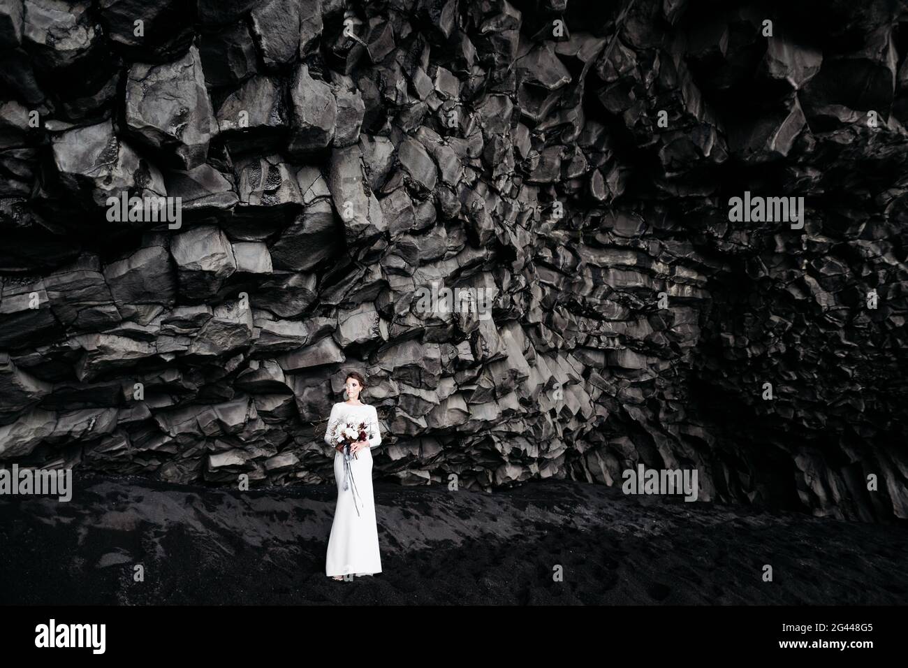 Destinazione Islanda matrimonio. La sposa in un abito di seta bianca con un bouquet tra le mani, si erge su sabbia nera, sulla spiaggia di Foto Stock