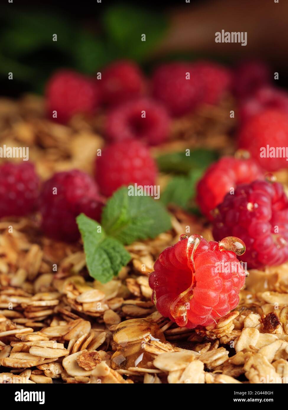 I lamponi si trovano sulla muesli con foglie di menta e gocce di miele. Foto verticale. Foto Stock