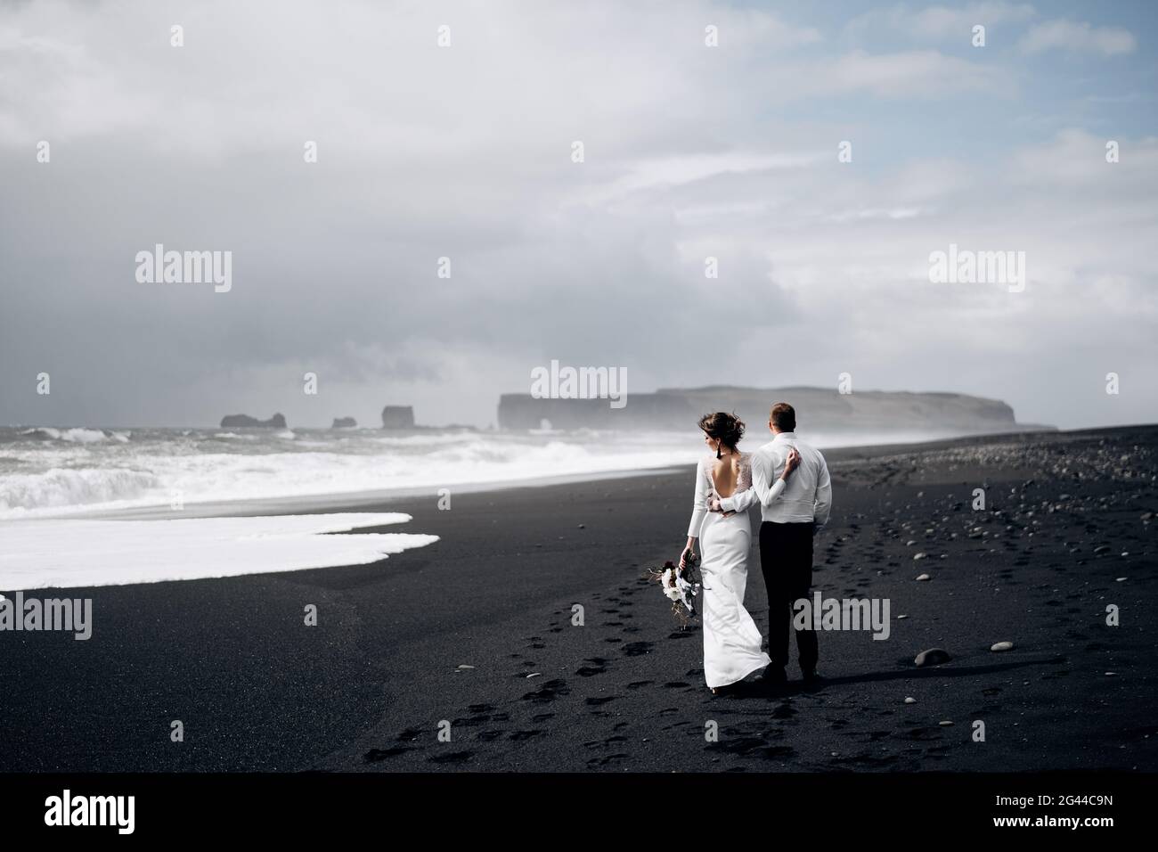Destinazione Islanda matrimonio. Una coppia di nozze sta camminando lungo la spiaggia nera di Vic. Spiaggia sabbiosa con sabbia nera sulle rive Foto Stock