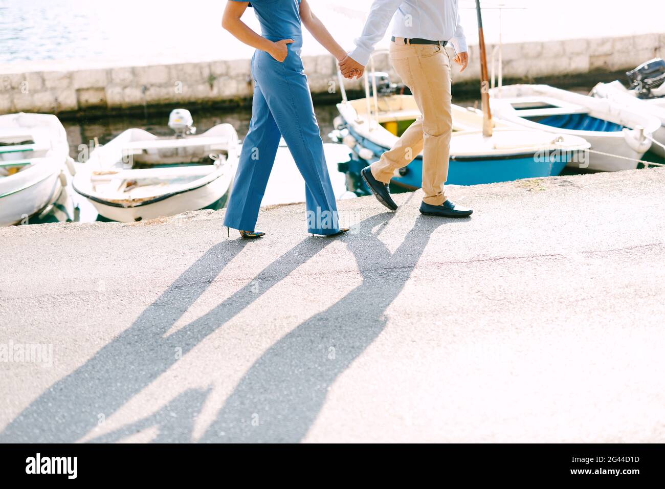 L'uomo e la donna camminano lungo il molo tenendo le mani sullo sfondo di yacht in una giornata di sole Foto Stock