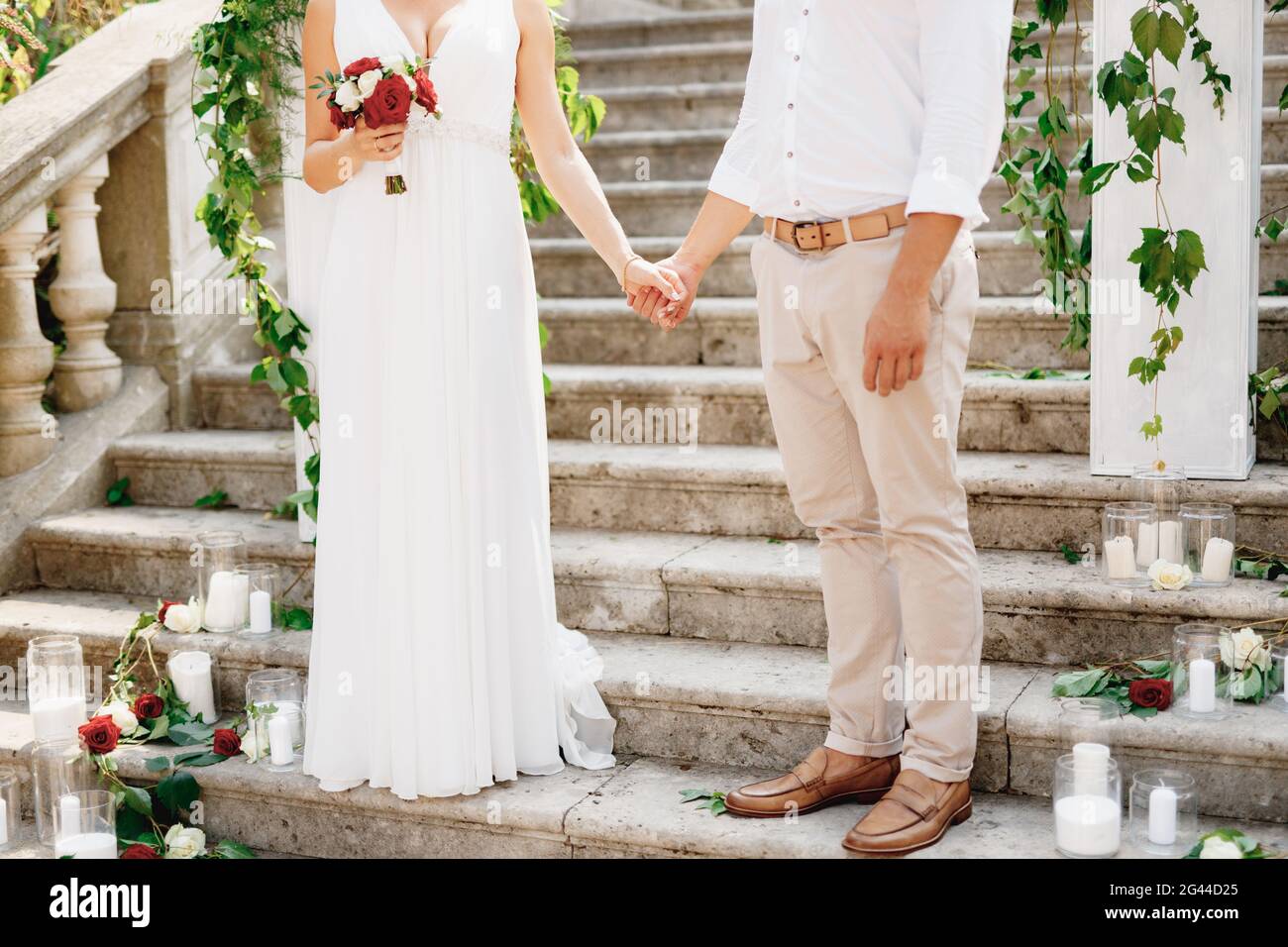 La sposa e lo sposo si trovano sulle scale della Natività della chiesa della Beata Vergine Maria a Prcanj e tengono le mani da vicino Foto Stock