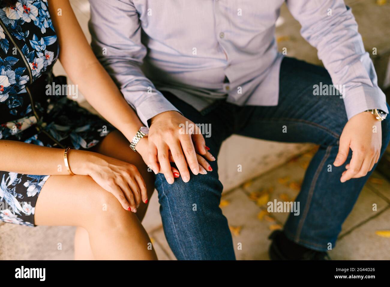 L'uomo in un vestito tiene le mani della donna dentro un abito colorato mentre si siede su una panchina Foto Stock L'uomo in un vestito tiene le mani della donna dentro un abito colorato mentre si siede su una panchina Foto Stock