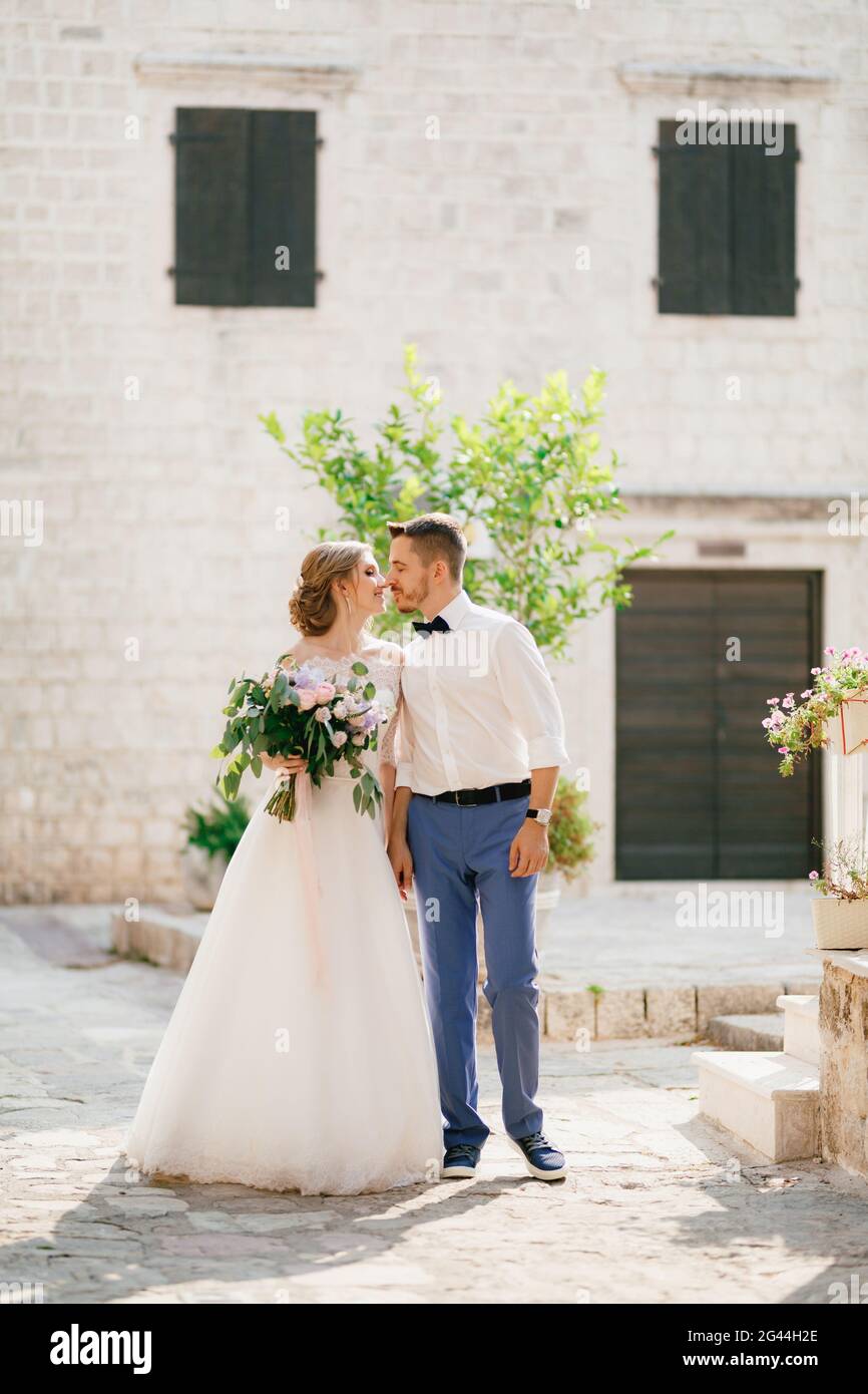 La sposa e lo sposo stanno tenendo le mani e baciando vicino a una bella casa in mattoni nella città vecchia di Perast, primo piano Foto Stock