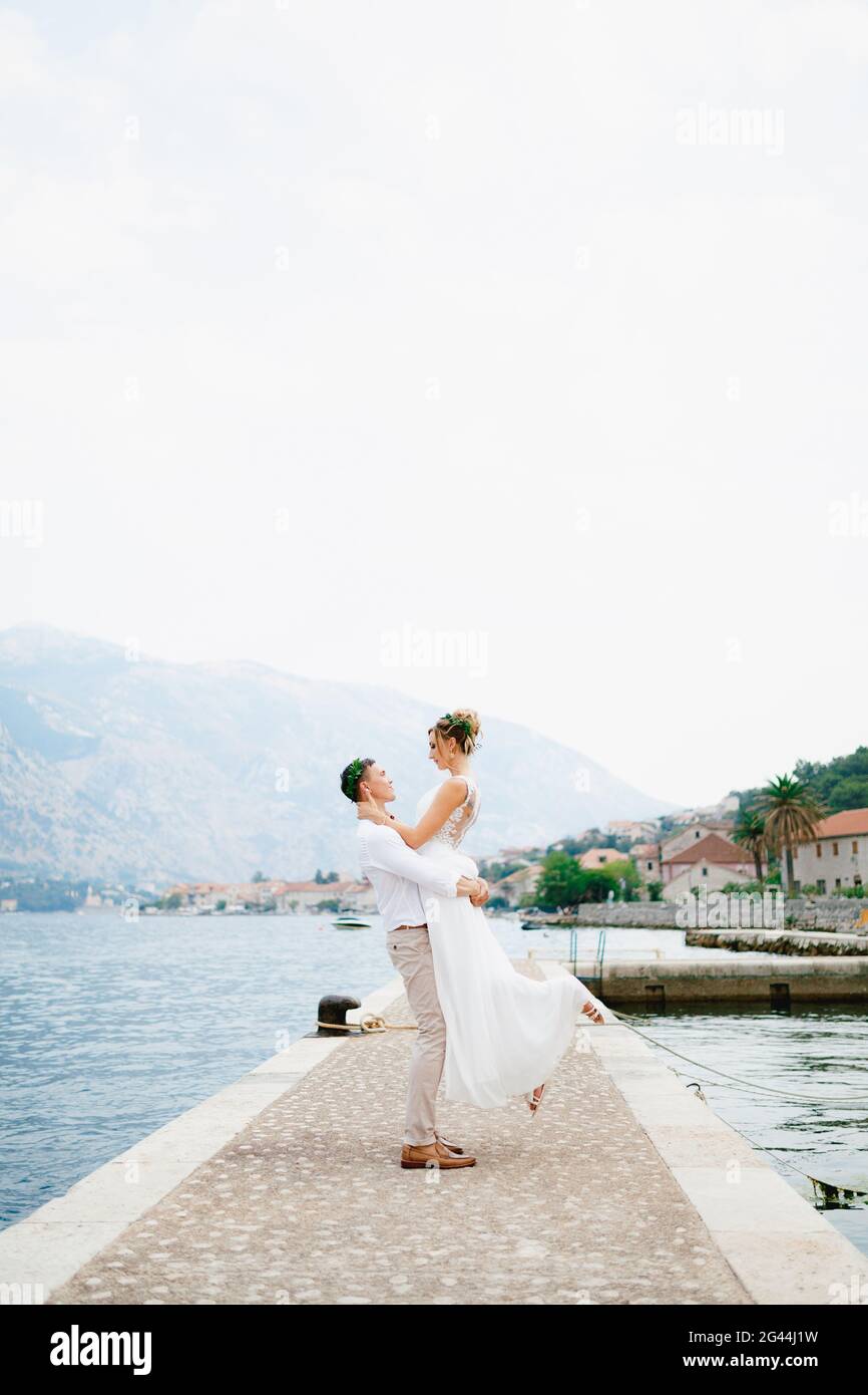 Lo sposo circoli la sposa tra le braccia sul molo nella baia di Cattaro vicino al vecchio accogliente città Foto Stock