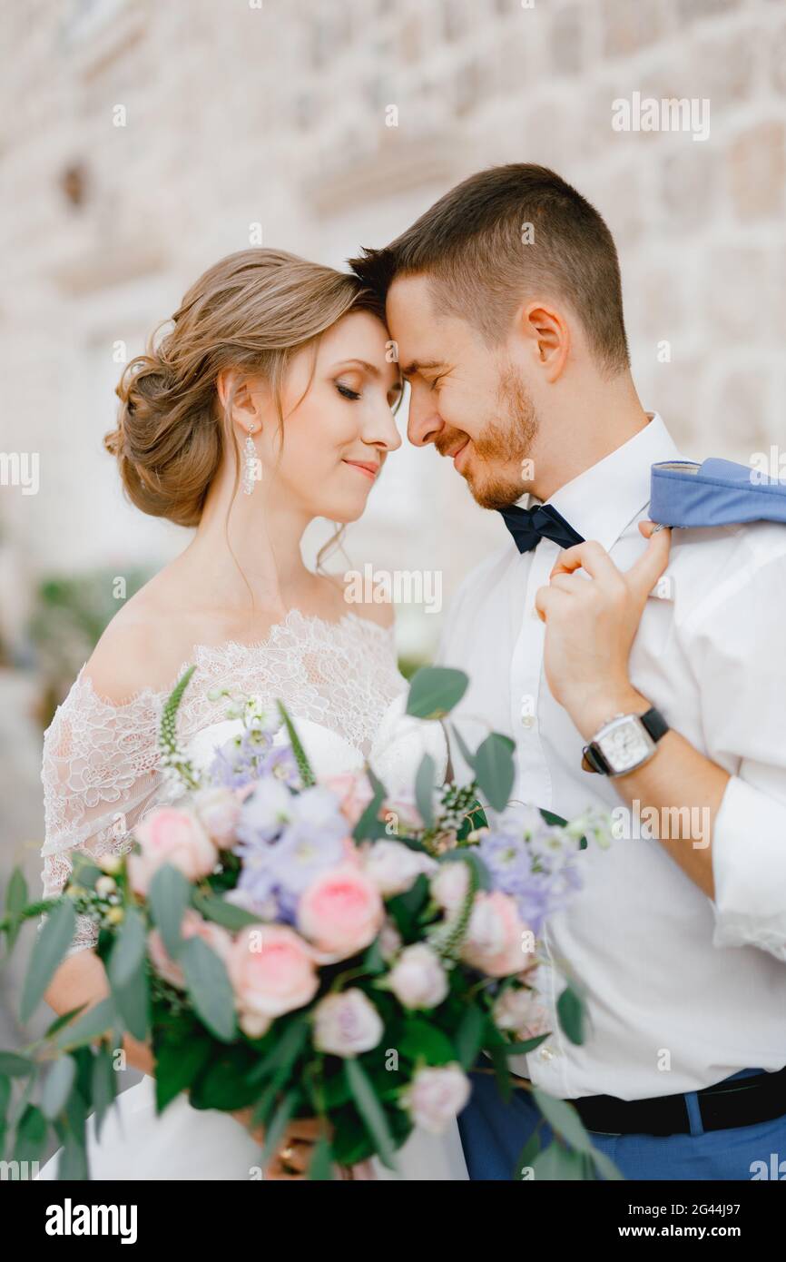 La sposa e lo sposo stanno abbracciando le mani vicino a una bella casa in mattoni nella città vecchia di Perast, primo piano Foto Stock