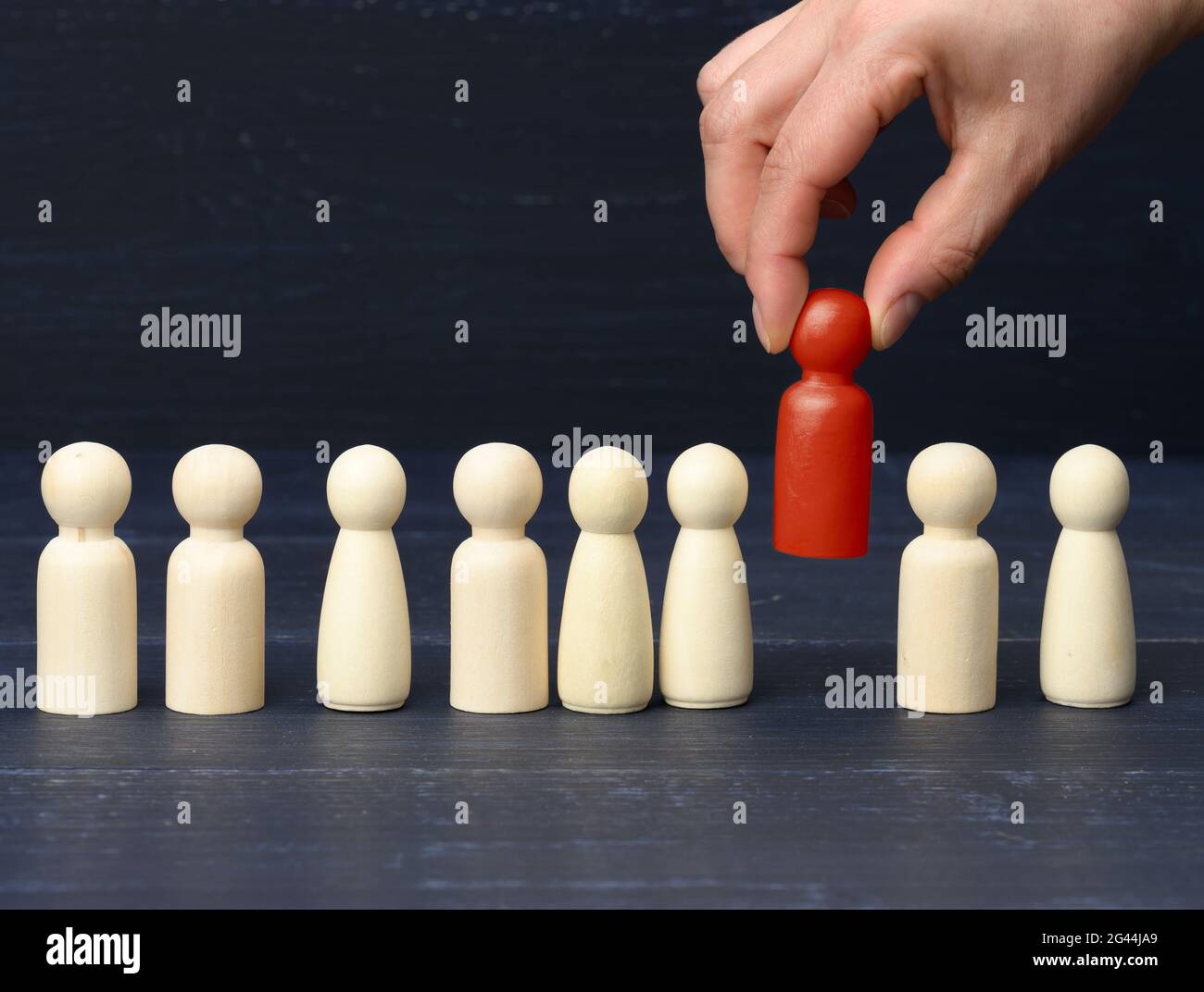 Una mano femminile tiene una figurina rossa di legno scelta dalla folla. Il concetto di trovare dipendenti di talento Foto Stock