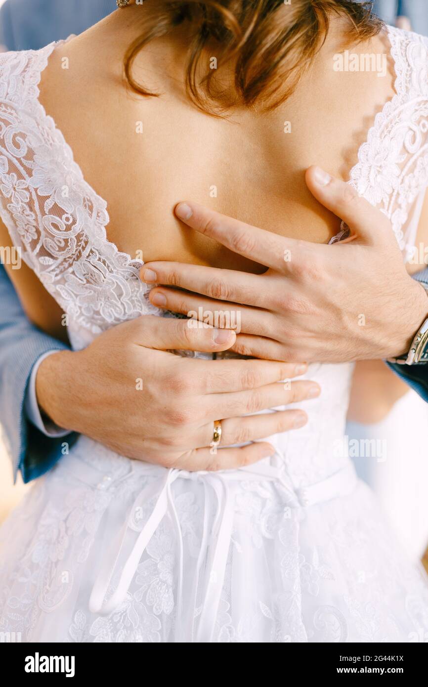 Mani ravvicinate di sposo abbraccio al punto vita in un abito in pizzo bianco. Foto Stock