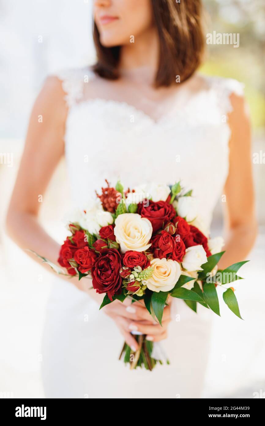 Sposa in un bel vestito bianco tiene un bouquet di rose rosse e rosa nelle mani Foto Stock