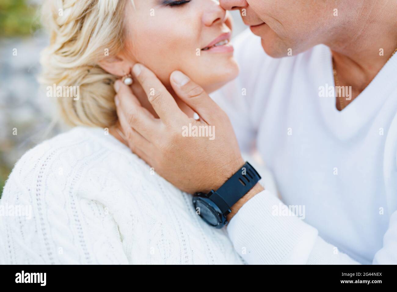 L'uomo in un maglione bianco e l'orologio nero bacia a. donna in un pullover bianco e bellissimi orecchini Foto Stock