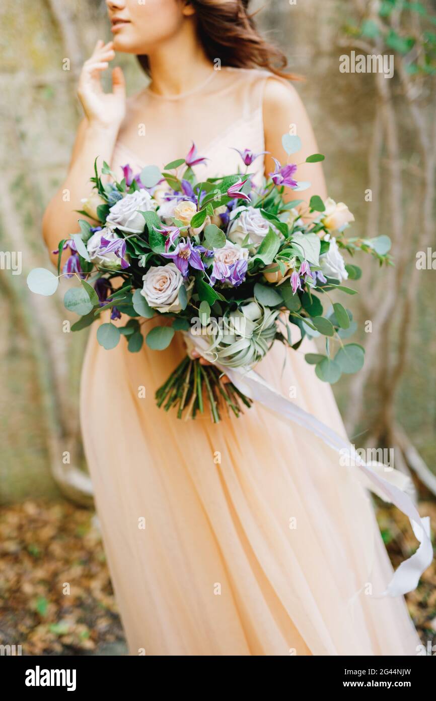 Mezzo-ritratto di una sposa in un abito beige e un bel bouquet di rose in mano Foto Stock