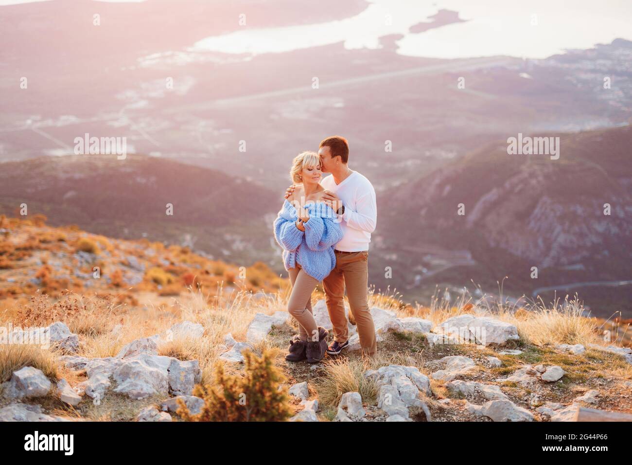 L'uomo abbraccia una donna in un maglione blu sulle spalle sullo sfondo del Monte Lovcen, baia di Kotor, Montenegro. Primo piano Foto Stock