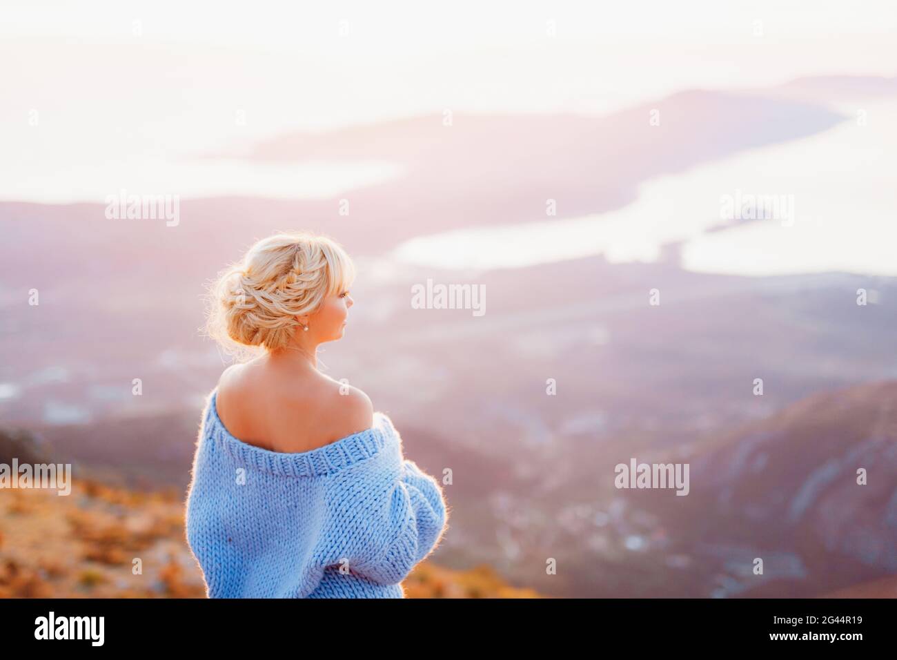 Donna in un pullover blu si alza e guarda il panorama del Monte Lovcen, Baia di Cattaro. Vista posteriore Foto Stock