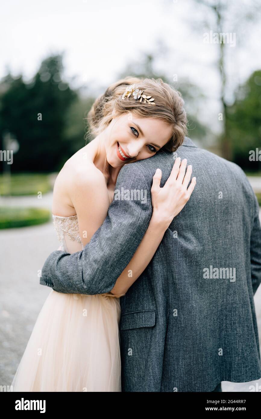 La sposa sorridente riposò la testa sulla spalla dello sposo abbracciandola nel parco. Lago di Como, Italia Foto Stock