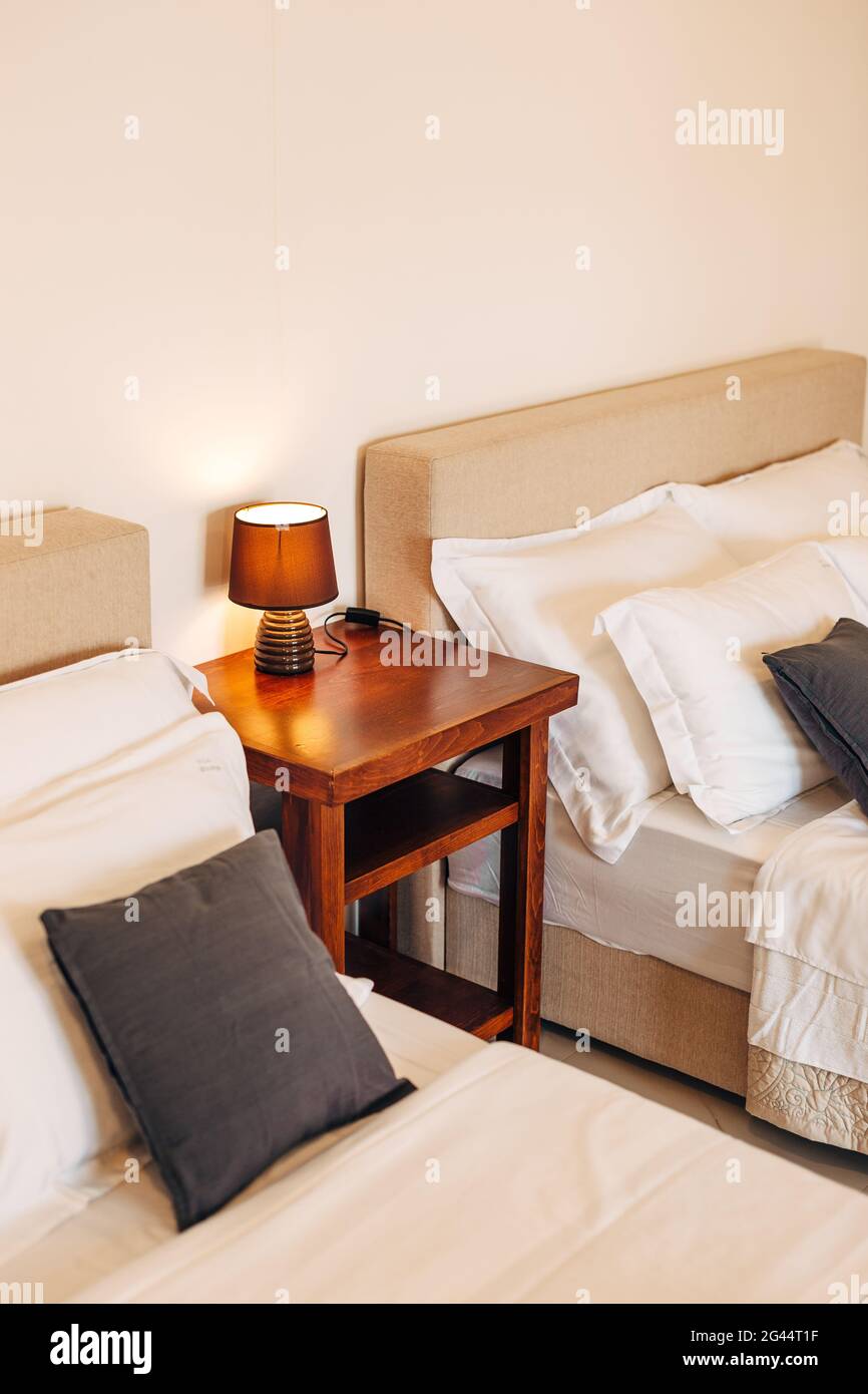 Due letti con cuscini bianchi e neri e un tavolo di legno con una lampada da notte tra loro. Foto Stock
