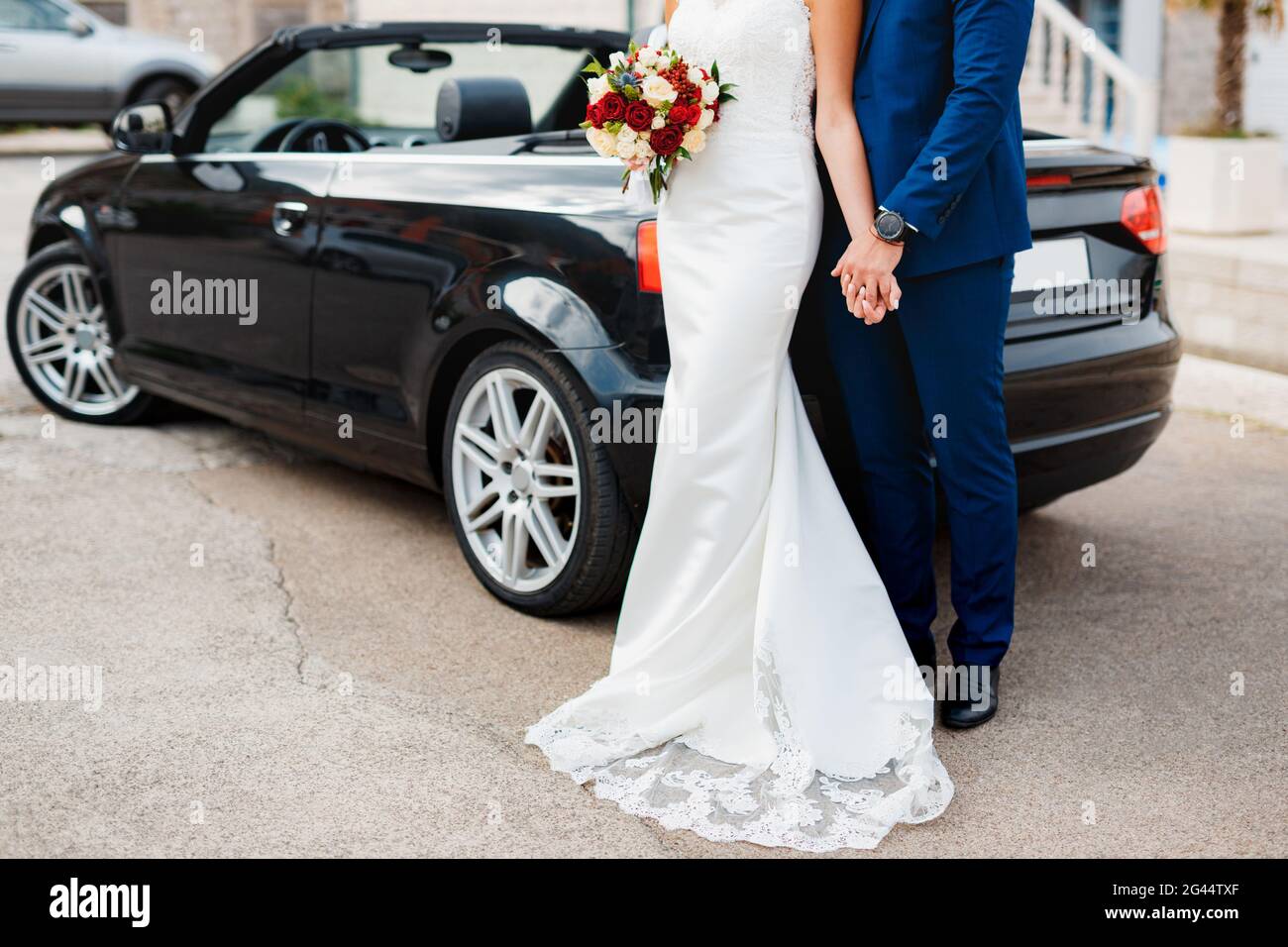 Lo sposo tiene la mano di sposa con un bouquet di fiori mentre si trova sulle lastre di pavimentazione sullo sfondo di un nero con Foto Stock