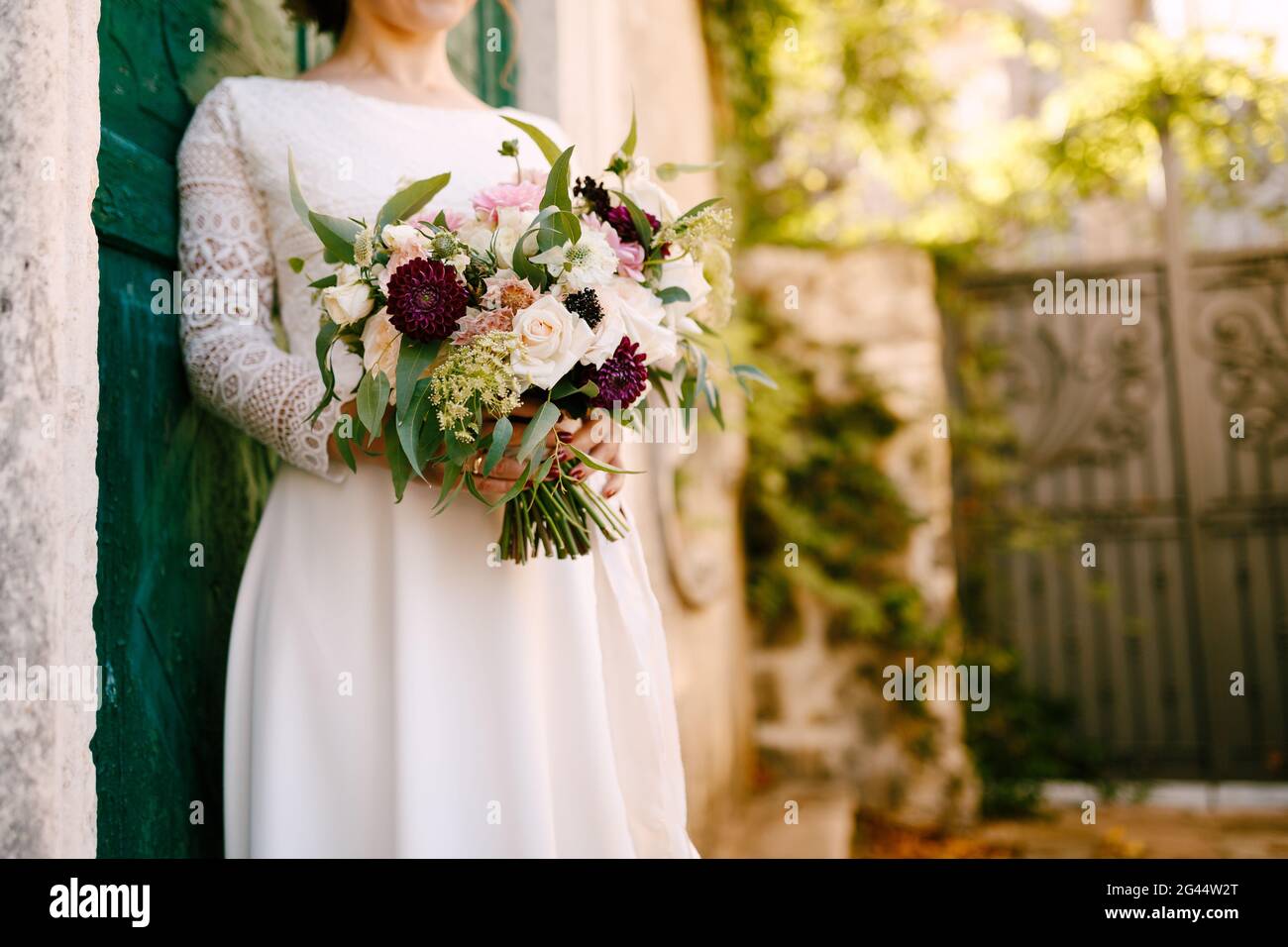 Sposa tiene in mano un bel bouquet di fiori appoggiandosi contro la porta verde dell'edificio Foto Stock