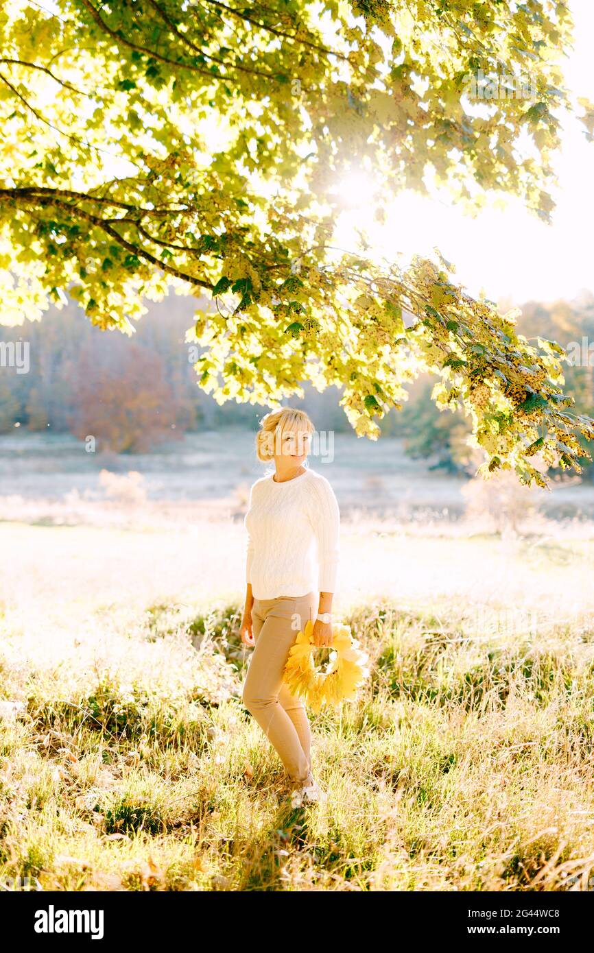 Donna che tiene una corona di foglie gialle sotto un albero in autunno foresta Foto Stock