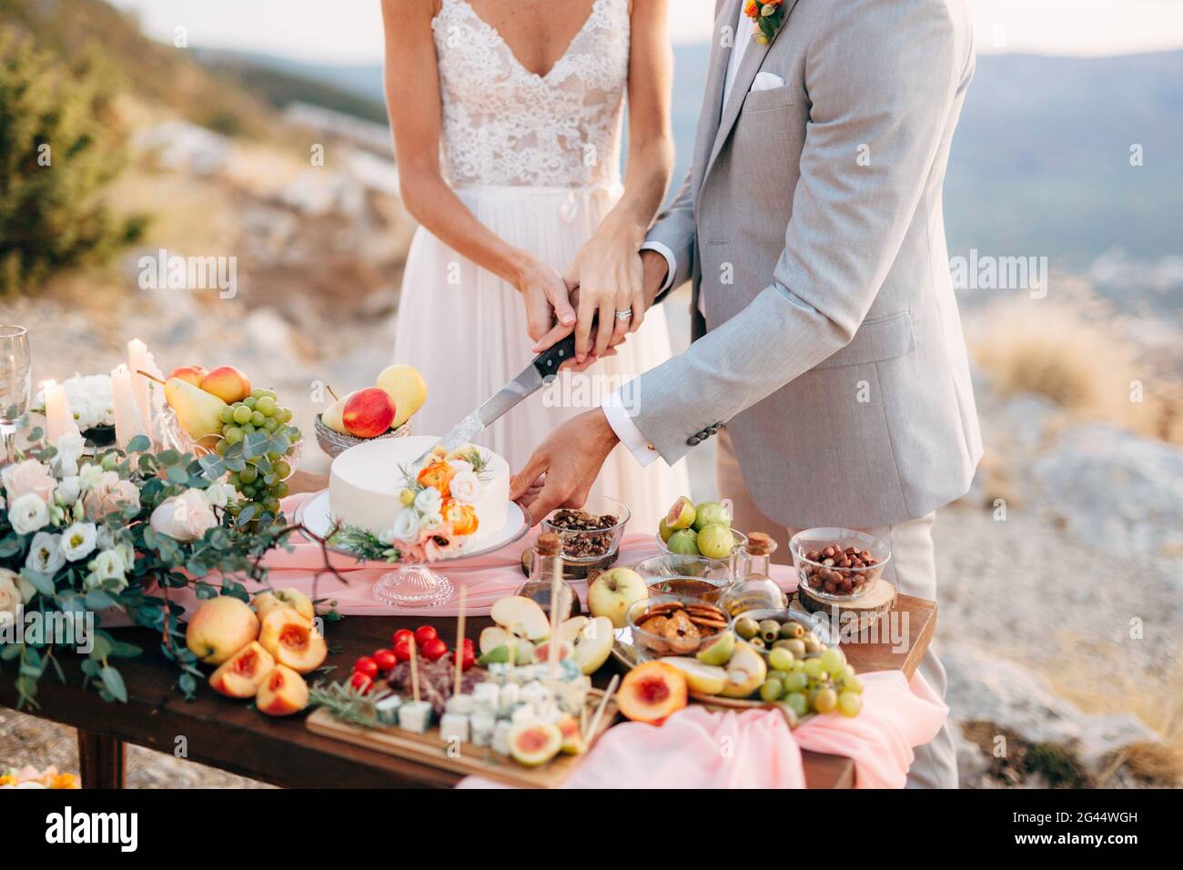 Lo sposo e lo sposo tagliano una torta durante un tavolo a buffet dopo la cerimonia nuziale sul Monte Lovcen, primo piano Foto Stock