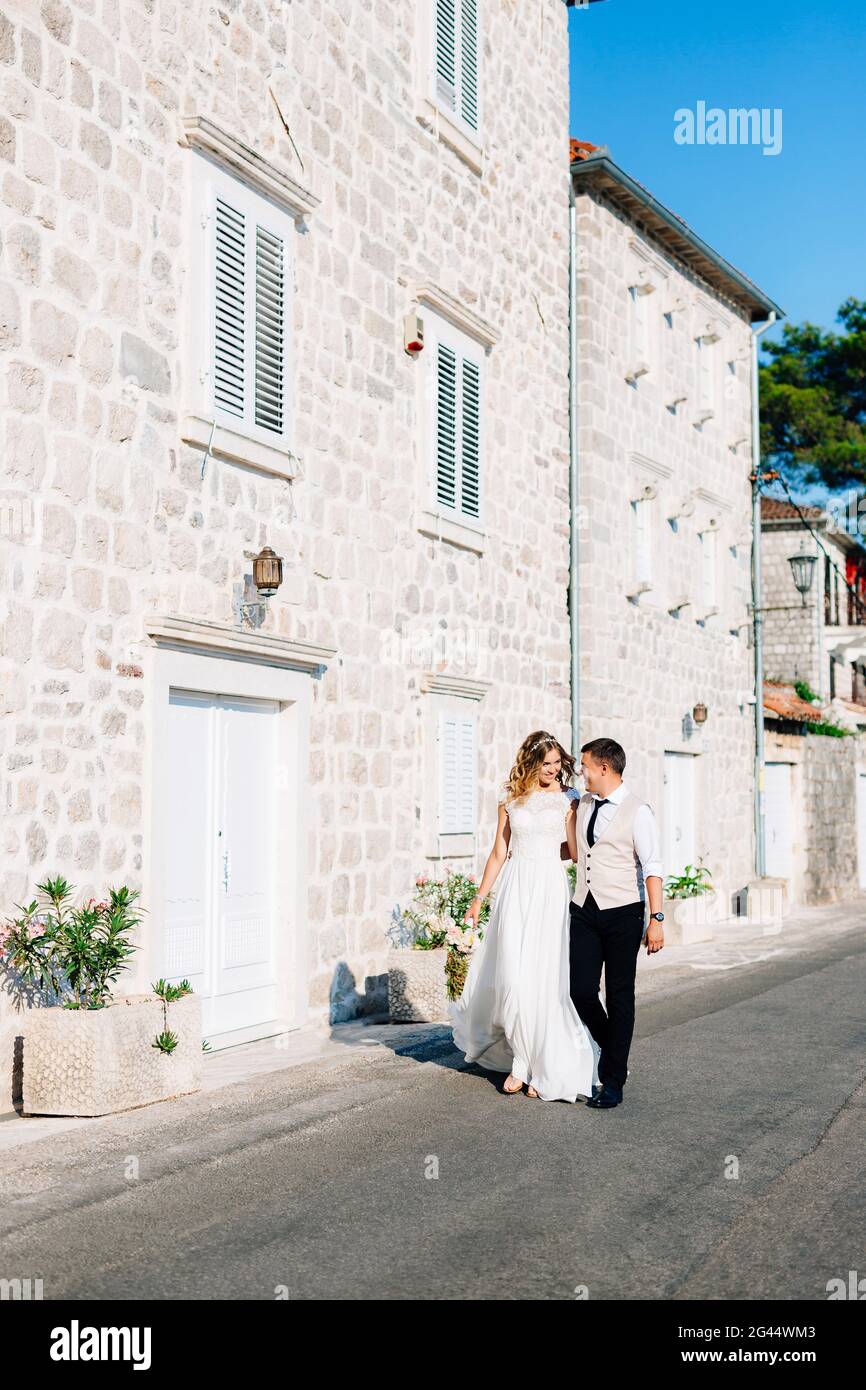 La sposa e lo sposo si abbracciano lungo il Strade di Perast vicino a case di mattoni bianchi Foto Stock