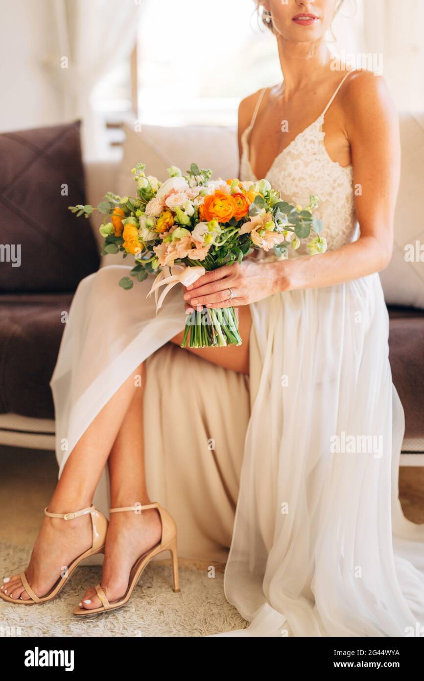 Una sposa in un abito da sposa e sandali con tacco alto si siede su un  divano in camera e può ospitare un matrimonio mazzo in mano Foto stock -  Alamy
